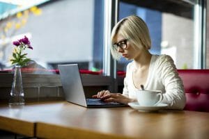 Young focused woman working on laptop with coffee cup on table in cafe, challenges of remote file access